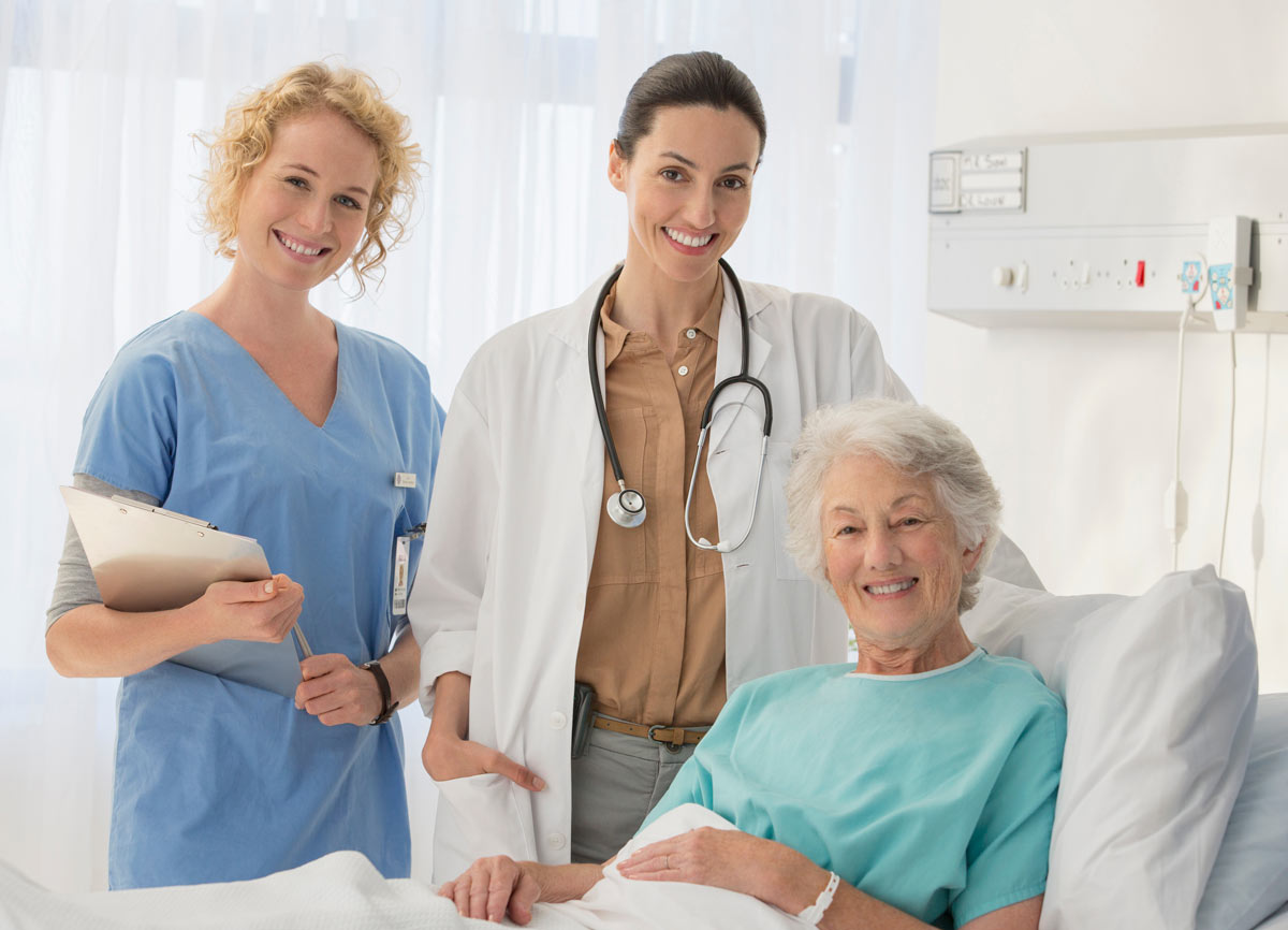 Kliniken & Therapiezentren: Ärztin und Pflegekraft betreuen ältere Patientin im Krankenhauszimmer – professionelle medizinische Versorgung und Patientenbetreuung.